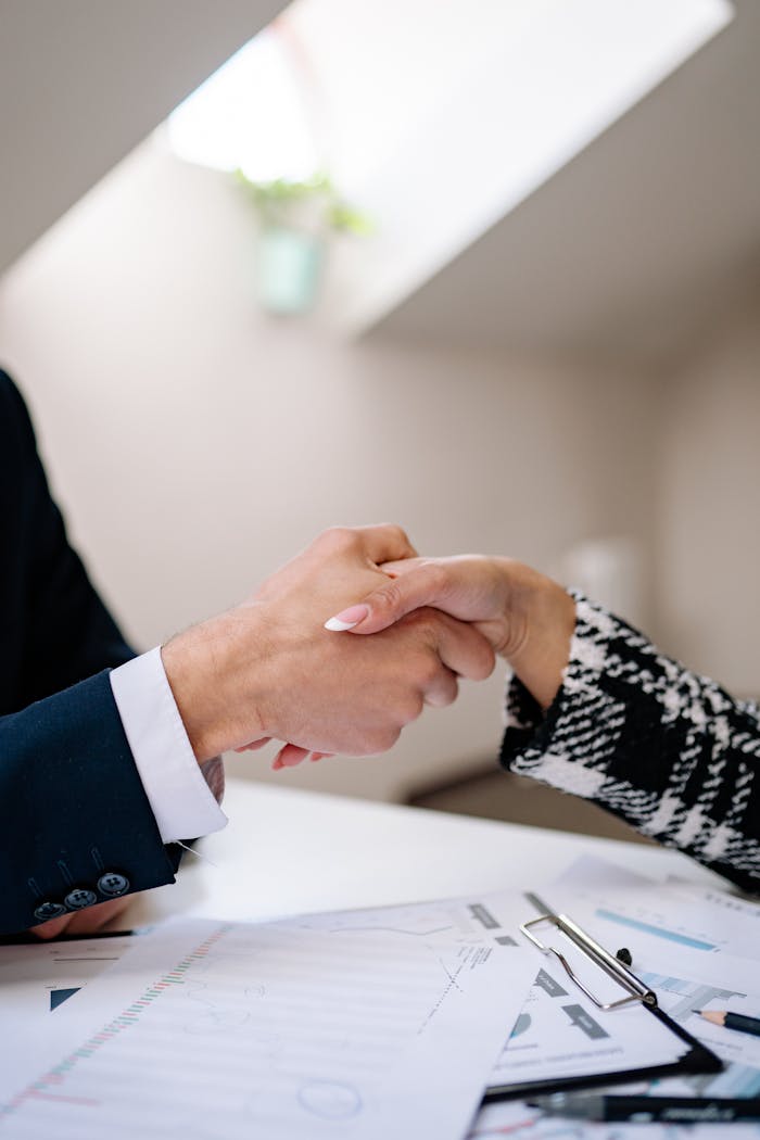 why-choose-us Close-up of a professional handshake between colleagues in a modern office setting, symbolizing agreement.